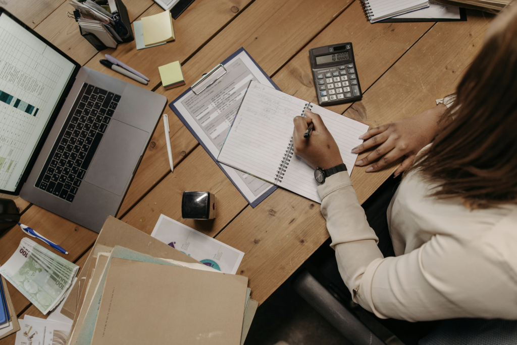 Woman writing in her notebook at a table with financial documents and a calculator, emphasizing trust accounting for property managers.