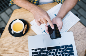 Hands using a phone next to a laptop and tea on a table, representing direct bookings setup.