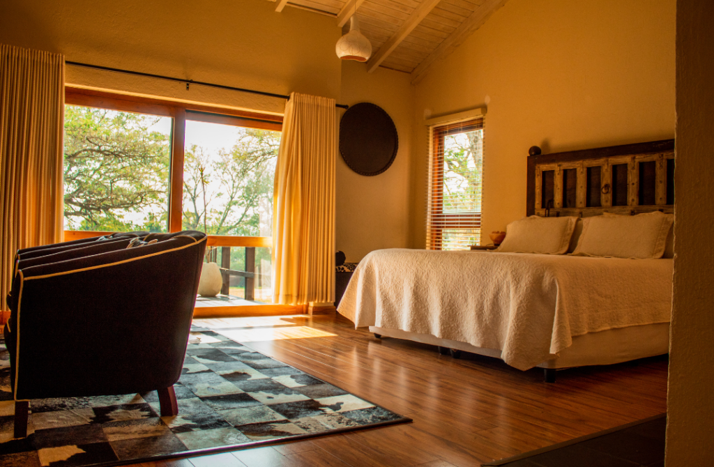 Cozy bedroom with a large bed, warm wooden decor, and a scenic view of trees through a window.