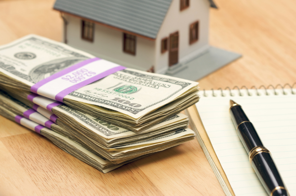 Stacks of cash, a small house model, and a notepad symbolizing property rental pricing decisions.