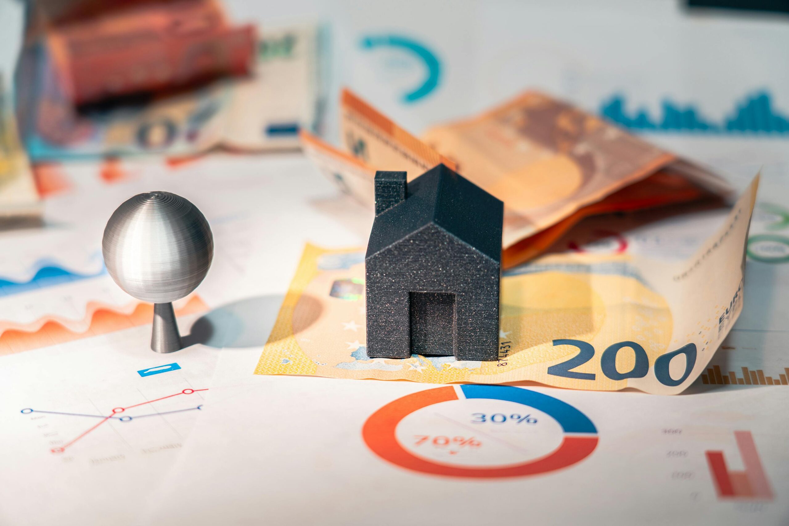 Miniature house and pin on financial charts and banknotes, illustrating strategies for managing and listing houses online effectively.