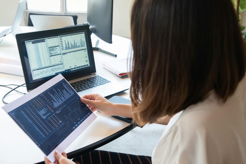 Woman reviewing printed charts while sitting in front of a laptop displaying data, focusing on Airbnb automation and performance analysis.