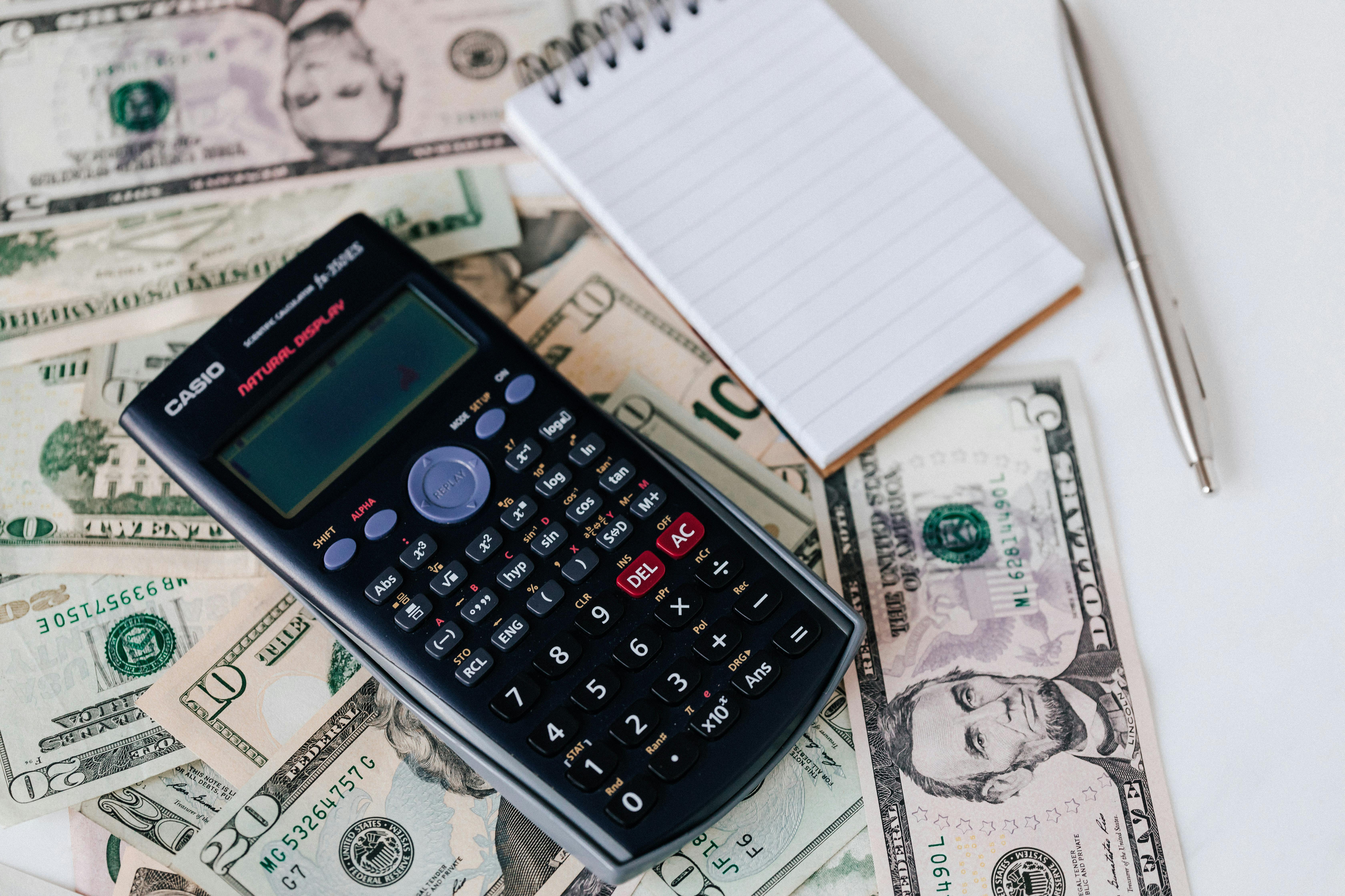 Calculator, notepad, and pen on a table with scattered dollar bills, illustrating tips on how to earn more profit on short-term rental property.