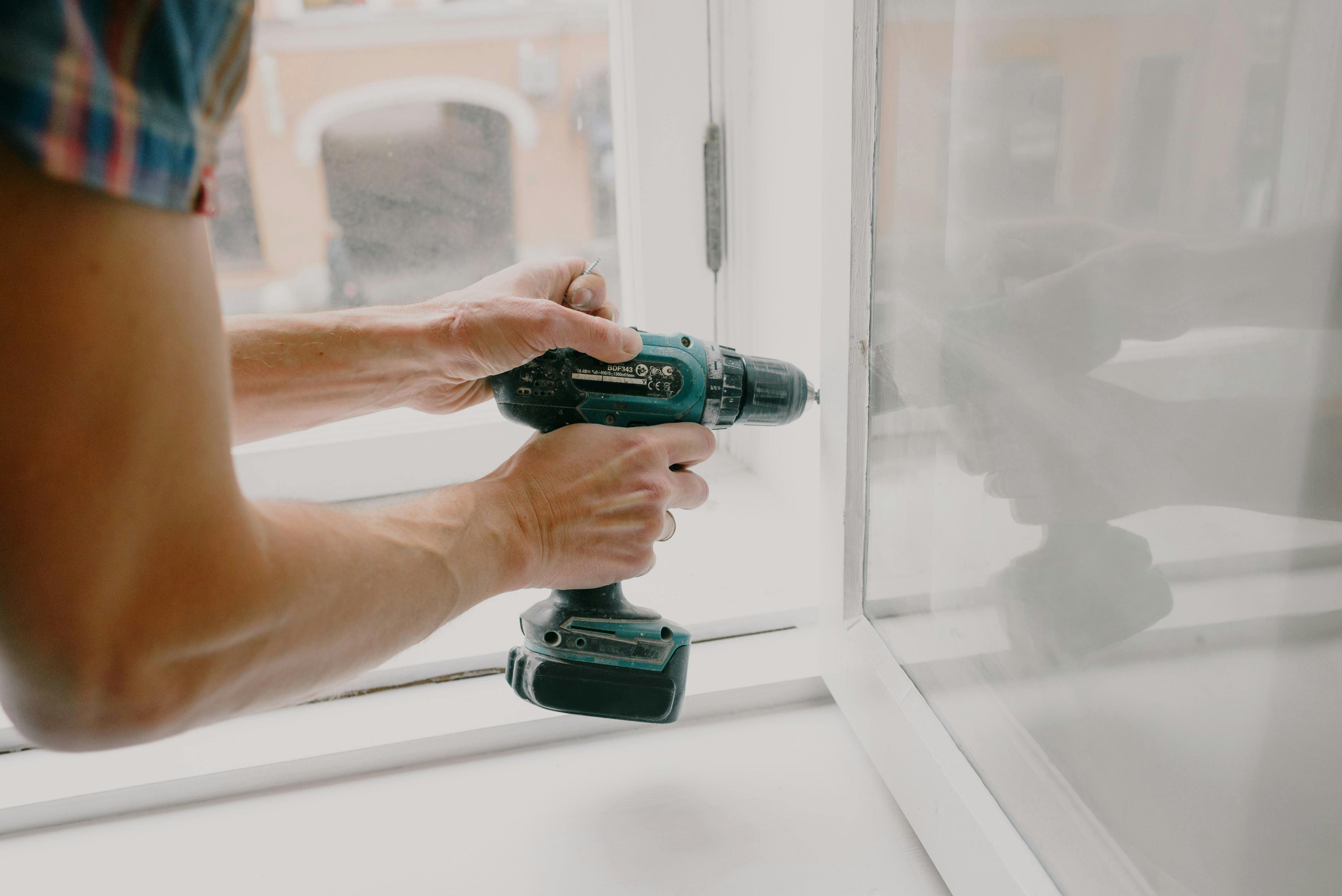 Person using a drill to repair a window, emphasizing the importance of upkeep when managing a vacation rental property.